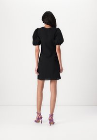 Czarna mini sukienka z bufkowymi rękawami, fakturowaną tkaniną i okrągłym dekoltem. Do tego fioletowe sandały na wysokim obcasie z paskami.