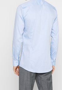 Jasnoniebieska koszula z długim rękawem o gładkiej fakturze i mankietach na guziki, z zaokrąglonym dołem i subtelnym pionowym wzorem na tkaninie.