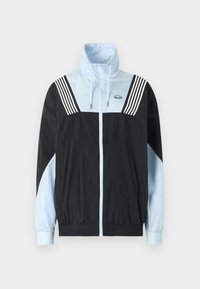 Fargeblokkert vindtett jakke i svart og lyseblå. Har glidelås foran, høy krage, og tre hvite striper på skuldrene. Mykt, lett materiale.