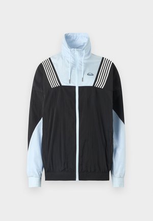 Corta-vento em blocos de cor em preto e azul claro. Apresenta um fecho éclair frontal, gola alta e três riscas brancas nos ombros. Material suave e leve.