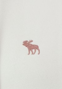 White fabric with a textured surface features a small, pink embroidered moose design on the left side.