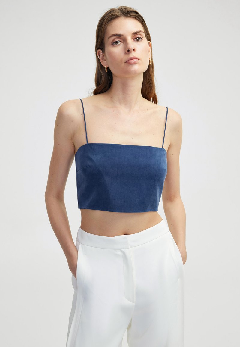 Marineblauw cropped top met dunne bandjes, gemaakt van een soepele, gestructureerde stof. Gecombineerd met witte high-waisted broeken. Eenvoudig en modern ontwerp.