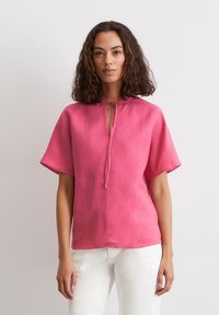 Rosa Leinenoberteil mit kurzen Ärmeln, mit einem V-Ausschnitt und einem Bindeband am Kragen. Glatte Textur, lockere Passform und gerader Saum.