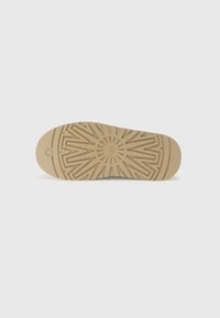 Tan rubber shoe sole with a textured, geometric pattern and circular logo at the center. Smooth edges and round toe for ergonomic design.
