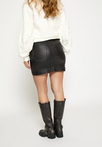 Sort mininederdel i imiteret læder med to baglommer, kombineret med knæhøje sorte læderstøvler med spænde og hældetalje.