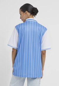 Lyseblå og hvid kortærmet skjorte med lodrette striber, krave og mesh-stof. Casual, afslappet pasform; markant sporty stil.