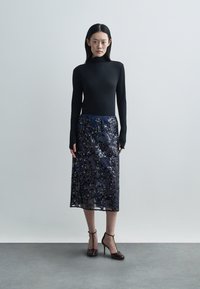 Čierny dlhý rukáv s rebrovanou textúrou v kombinácii s tmavomodrou midi sukňou z kvetinovej čipky. Lodičky s remienkami okolo členkov.