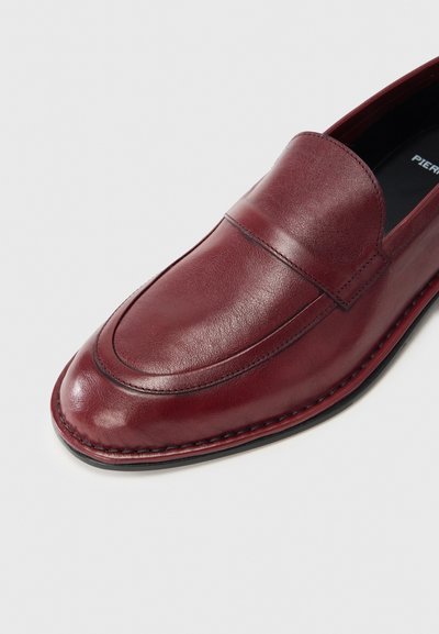 Μπορντό δερμάτινα μοκασίνια με ομαλή υφή, στρογγυλερή μύτη και λεπτομέρεια ραφής κατά μήκος της σόλας. Στο εσωτερικό διαθέτουν μαύρη επένδυση με λογότυπο.