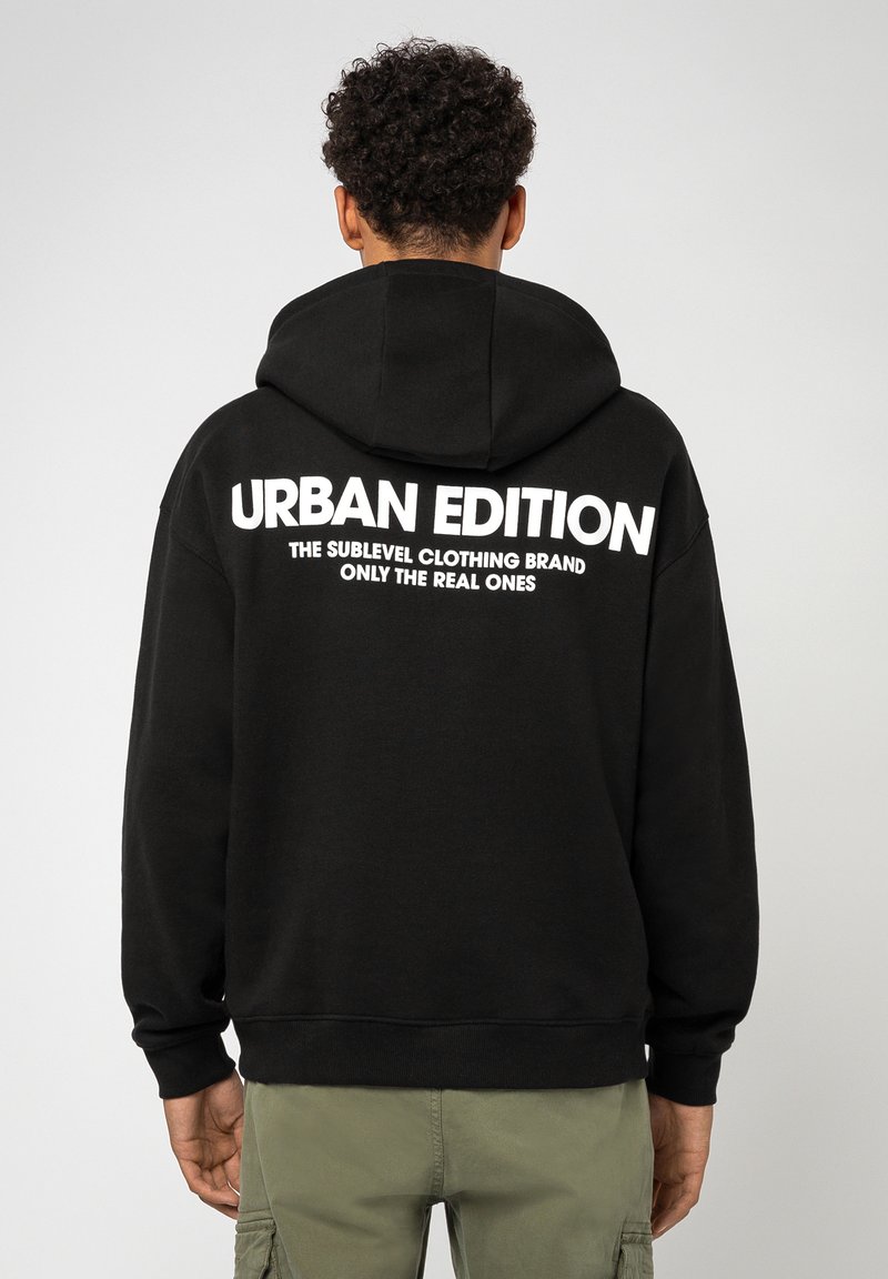 Schwarzer Hoodie mit Kordelzugkapuze, mit weißem Text auf der Rückseite: "URBAN EDITION DIE SUBLEVEL KLEIDUNGSSEITE NUR FÜR DIE WAHREN."
