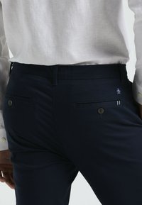 Marineblauwe pantalon van gladde stof, met een slim fit, twee achterzakken met knopen en een klein logo op de tailleband.