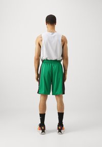 Žalios sportinės šortai su juodais akcentais, derinami su laisvai krentančiu baltu marškinėliu. Audinys su tekstūra, elastingas juosmuo ir juodi kojinės iki kulkšnies.