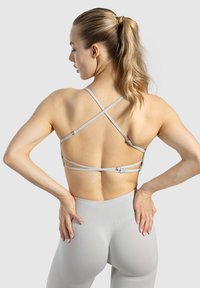 Hellgrauer Sport-BH mit überkreuzten Trägern, verstellbarem Zubehör und nahtlosem Design, kombiniert mit passenden hochgeschnittenen Leggings.