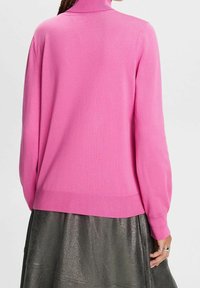 Fuchsia roze lange mouwen trui met een hoge kraag. Geribde manchetten en zoom, glad gebreide textuur, gecombineerd met een metallic donkere rok.