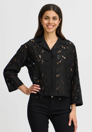 Blouse en dentelle noire avec un col, fermeture à boutons à l'avant, coupe courte et manches trois-quarts ornées de motifs floraux et de textures.