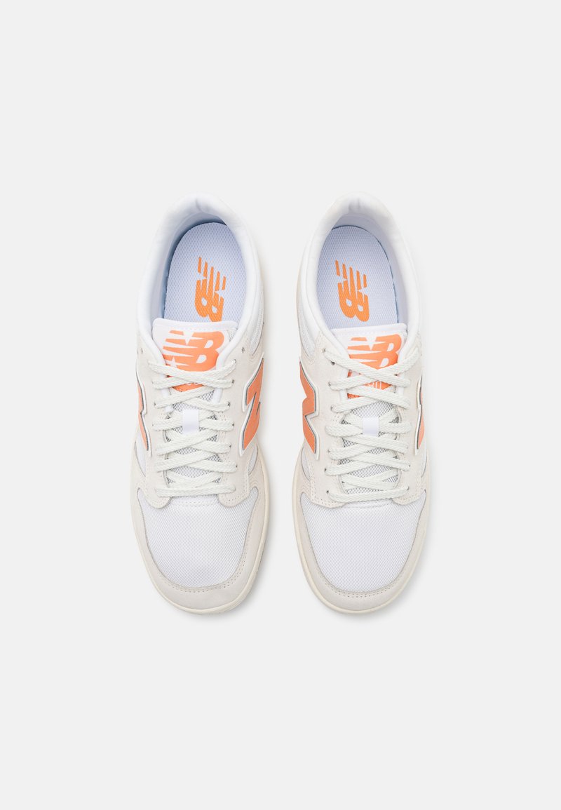 Chaussures de sport blanches en matériaux en maille et en cuir. Présentent un logo "N" orange et des lacets, avec des semelles intérieures rembourrées et des semelles texturées.