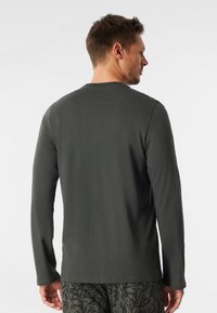 Camicia grigia a maniche lunghe realizzata in un tessuto morbido, con scollatura rotonda e vestibilità rilassata, abbinata a pantaloni corti scuri con fantasia.