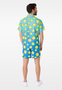 Ensemble en bleu comprenant un t-shirt à manches courtes et un short, avec un motif de smiley jaune. Fabriqué à partir d'un tissu léger, idéal pour un style décontracté.