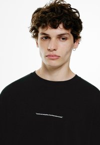 Sort bomulds t-shirt med rund hals og korte ærmer, med hvid tekst trykt på fronten: "Lektioner er overalt, hvis du ved, hvor du skal lede."