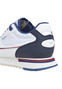 Pantofă sport albă cu accente bleumarin, având un brâu din piele netedă, un călcâi texturat și un mijloc colorat în dungi. Logo și anul "1973" pe călcâi.