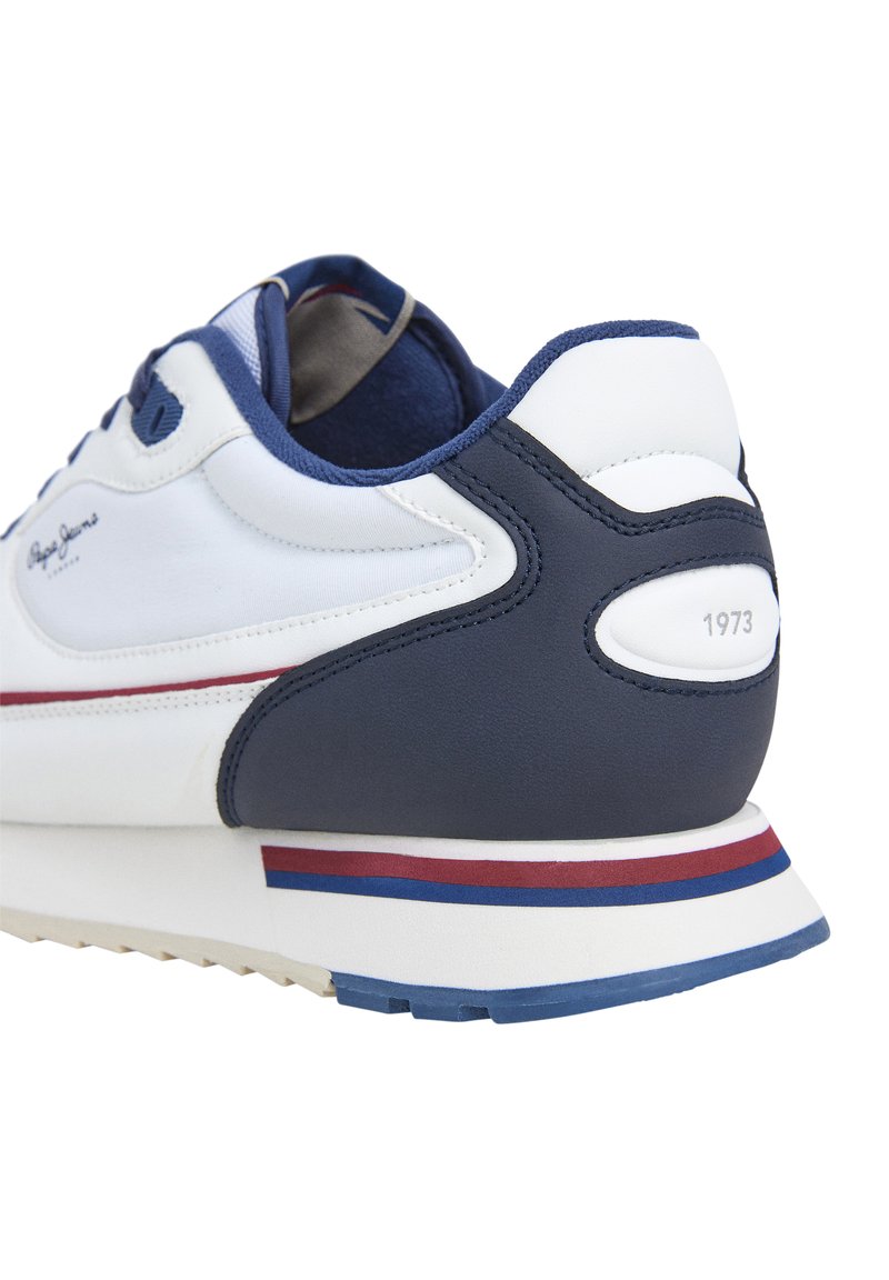 Zapatilla deportiva blanca con acentos en navy, que presenta una parte superior de cuero suave, un talón texturizado y una entresuela de rayas coloridas. Logotipo y año "1973" en el talón.