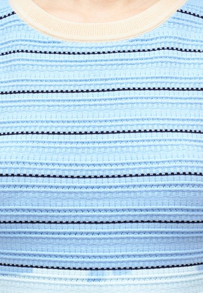 Κοντινή λήψη ενός ανοιχτού γαλάζιου πουκάμισου με οριζόντιες μαύρες και σκουρόχρωμες μπλε ρίγες και μπεζ γιακά στο άνω μέρος του στήθους ενός ατόμου.