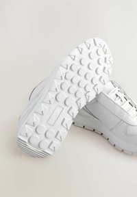 Hvide sneakers med en tekstureret læderoverdel og en robust gummisål med cirkulære og trekantede mønstre for bedre greb.