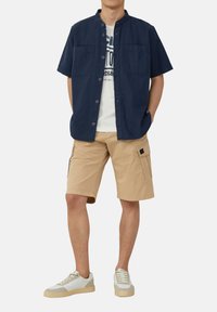 Korte mouwen marineblauwe button-up shirt, beige cargoshorts en witte sneakers met grijze accenten. Beschikt over zakken en heeft een casual pasvorm.