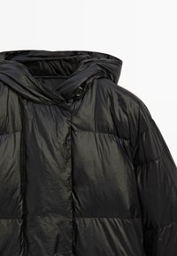 Černá péřová bunda s lesklým, reflexním povrchem, vybavená kapucí a knoflíkovým zapínáním. Design zahrnuje prošívaný vzor pro izolaci.