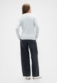 Svetlo sivi pleteni pulover z ohlapnim krojem, kombiniran z visokim pasom in širokimi črnimi kavbojkami. Bela športna obutev dopolnjuje videz.