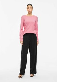 Pink long-sleeve sweater with a round neck, paired with high-waisted black trousers. Soft texture, tailored fit, and minimalist design.