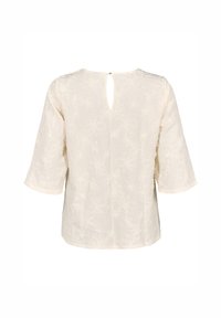Blusa cremosa con texture, maniche 3/4, caratterizzata da uno scollo a chiave sul retro e un motivo floreale, realizzata in tessuto leggero.
