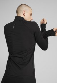 Zwart sportief shirt met lange mouwen, voorzien van een hoge kraag, aansluitend ontwerp en naaddetails, met duimgaten aan de mouwuiteinden.
