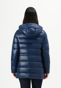 Mørkeblå puffjakke med hette, med en glansfull overflate, horisontal søm og mellomlang lengde.