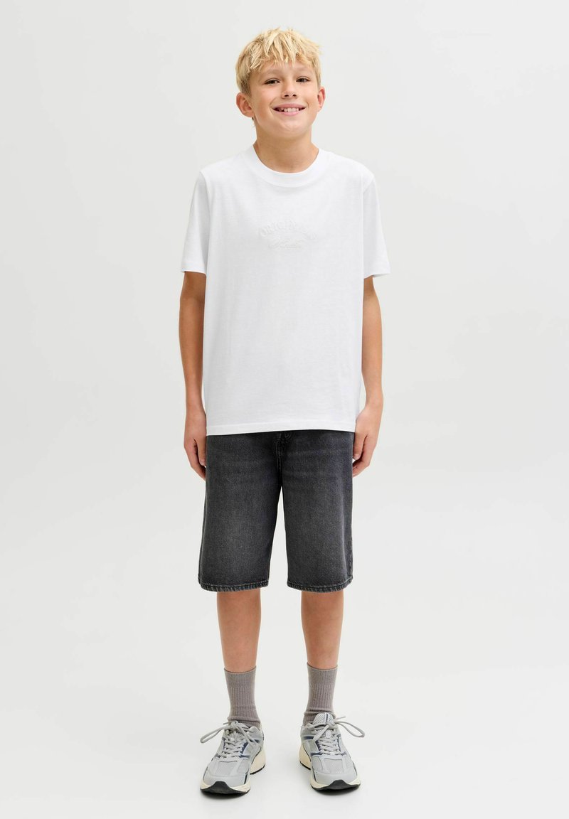 Camiseta blanca de manga corta con un logo texturizado, combinada con pantalones cortos de mezclilla gris oscuro y zapatillas gris claro. Look casual, colores neutros.