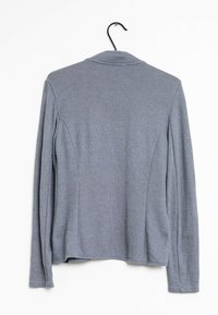 Maglione grigio chiaro a maniche lunghe appeso a una gruccia nera su sfondo bianco, visto da dietro.
