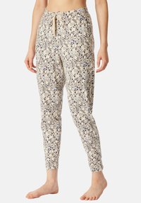 Pantalons à motifs floraux en beige clair avec des dessins bleus et bleu marine foncé. Tissu doux avec taille à lacet. Ajustés aux chevilles.