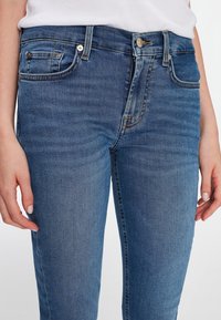 Jeans de denim en azul claro con un diseño ajustado, estilo de cinco bolsillos, costuras visibles y un cierre de botón en la cintura.