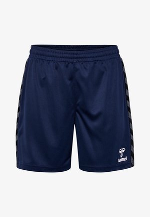 Persoon draagt marineblauwe sportshorts met een zij-chevronpatroon, zwarte sneakers, witte sokken en een marineblauwe top met lange mouwen.