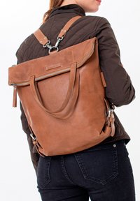 Brauner Leder-Rucksack mit verstellbaren Riemen, Reißverschluss oben und zwei Griffen; verfügt über eine Fronttasche und eine schlichte Textur.