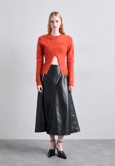 Pulover tricotat roșu pufoș cu decolteu în V, asortat cu o fustă neagră din piele, cu talie înaltă și fermoare. Pantofii negri cu toc completează look-ul.