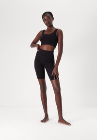 Zwart sportoutfit bestaande uit een fitted crop top en high-waisted bike shorts, gemaakt van glad materiaal met een naadloos ontwerp.