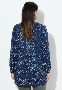 Tunique blu navy con motivi a cuore bianchi, maniche lunghe, design con pieghe sul retro e scollatura rotonda. Tessuto morbido e leggero.
