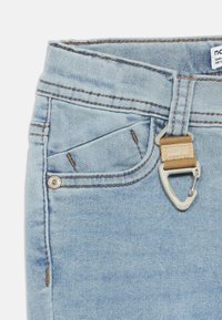 Οι ανοιχτό μπλε τζιν παντελόνια διαθέτουν ασημένιο κουμπί και θηλιά ζώνης από ταμπά υφασμάτινη ταινία. Το ύφασμα έχει μαλακή υφή με αντίθετες ραφές.