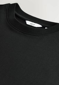 Sort afslappet t-shirt lavet af blødt, tekstureret stof. Har en rund halsudskæring og en label med teksten "NEXT." Enkel og alsidig design.