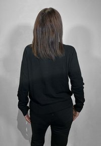 Maglione nero a maniche lunghe con vestibilità rilassata, realizzato in materiale lavorato a maglia testurizzato, abbinato a pantaloni neri. Il capo ha un design semplice.