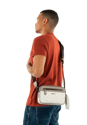 Sac bandoulière en beige et gris avec logo, poche zippée et motif texturé. La bandoulière ajustable contraste avec la surface du sac.