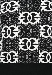 Sweter dziergany w czarno-białym geometrycznym wzorze z motywami kwiatowymi i owalnymi, teksturowana tkanina oraz ściągacz u dołu.