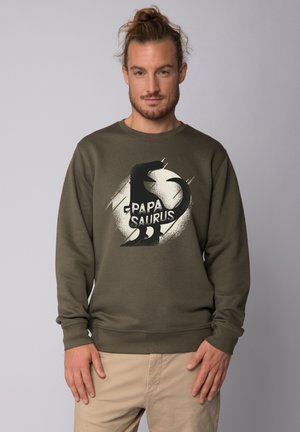 Olivgrüner Sweatshirt mit einem runden Grafikmotiv, das einen Dinosaurier zeigt, und dem Schriftzug "Papa Saurus" in fetten schwarzen Buchstaben. Glatte Textur, Rundhalsausschnitt-Design.