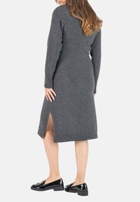 Robe tricotée gris à manches longues avec fentes latérales, poignets côtelés et longueur mi-mollet. Associée à des chaussures en cuir verni noires.