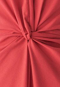 Koralinvärgad tyg med en mjuk textur, med tvistade knoppar i mitten och flödande draperier som skapar en elegant design.